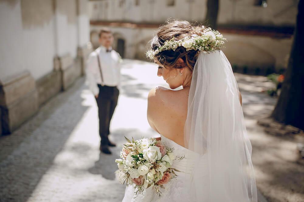 Young bride in veil and flower garland, groom standing in the distance