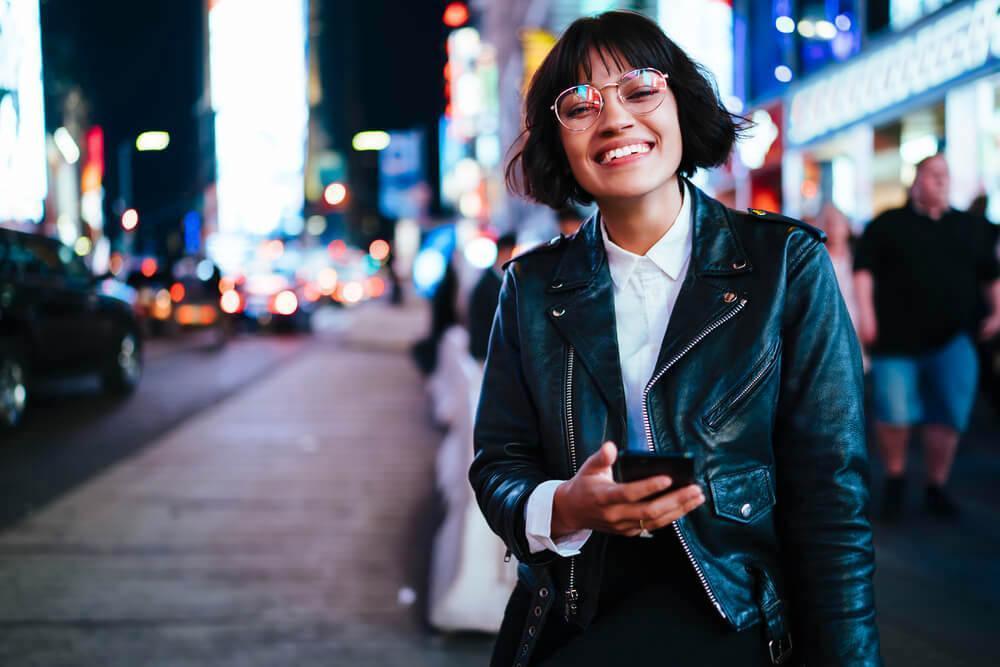 Happy smiling woman with glasses and a leather jacket in the city