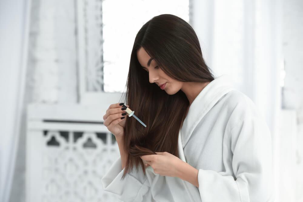 Woman applying hair serum to long straight hair