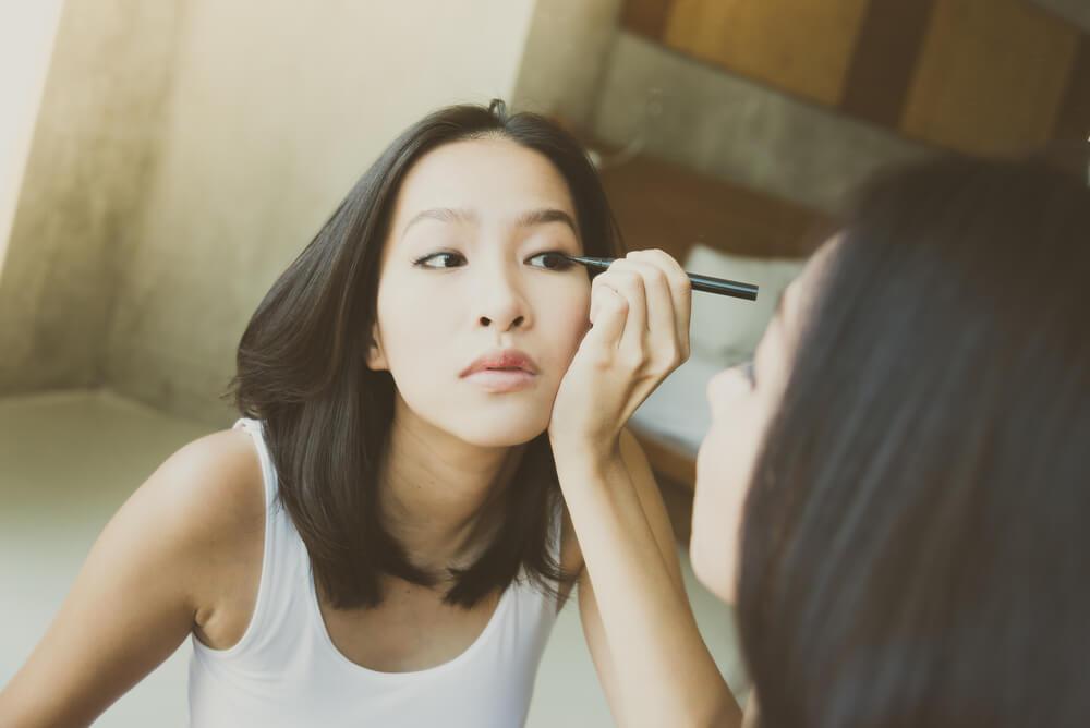 Woman applying eyeliner in front of mirror