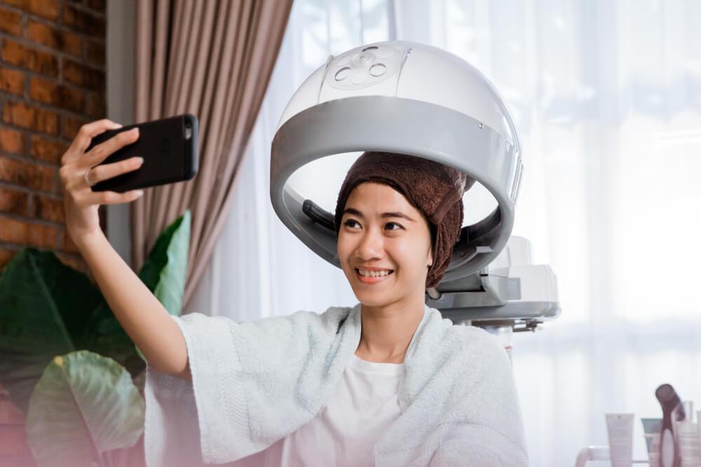 Woman taking selfie while steaming hair at home